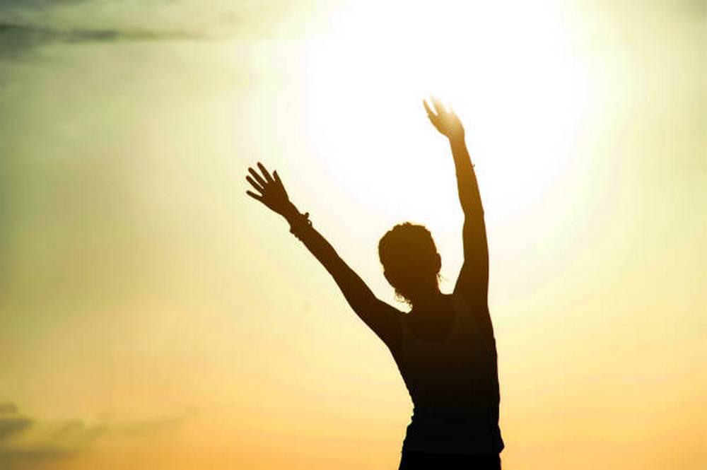 Free happy woman raising arms watching the sun in the background at sunrise